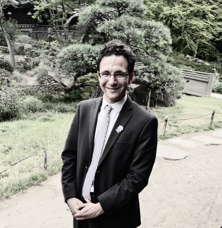 Fred smiling in a dark suit, standing in a Japanese garden.